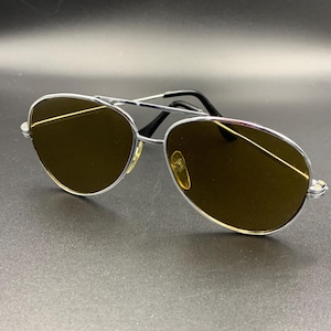 May include: Silver aviator sunglasses with brown lenses. The sunglasses have a classic design and are perfect for protecting your eyes from the sun.