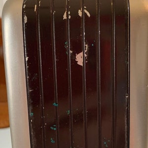 May include: Close-up of a silver and black vintage radio with a textured, grooved panel. The panel has some paint chips and scratches.