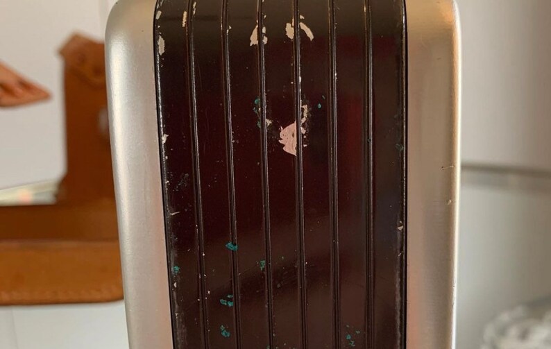 May include: Close-up of a silver and black vintage radio with a textured, grooved panel. The panel has some paint chips and scratches.