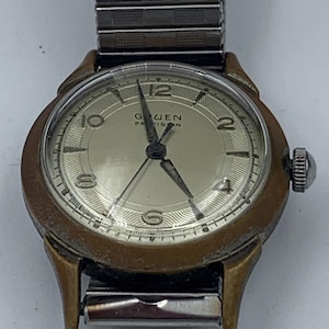 May include: A gold-toned Gruen Precision wristwatch with a white face and black hands. The watch has a silver metal band.