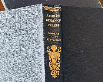 Può includere: Un libro nero con lettere dorate sul dorso. Il titolo è "A Child's Garden of Verses" di Robert Louis Stevenson. Il libro ha un disegno decorativo dorato sul dorso.
