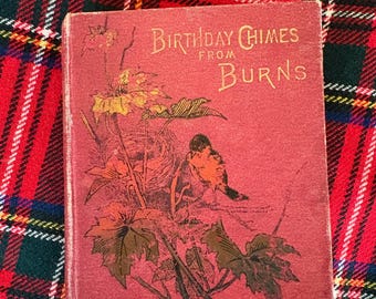 Pode incluir: Um livro vintage intitulado "Birthday Chimes From Burns" com uma capa vermelha. A capa apresenta uma ilustração de um pássaro empoleirado em um galho com folhas e o título em letras douradas. O livro está sobre um fundo xadrez vermelho e verde.