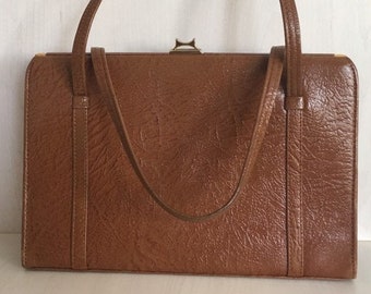 May include: A brown leather handbag with a gold clasp and a top handle. The bag has a textured surface and a rectangular shape.