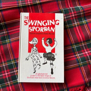 May include: A book titled "The Swinging Sporran" with illustrations of dancing figures, set against a red and green tartan background. The book is a guide to Scottish reels and country dances.
