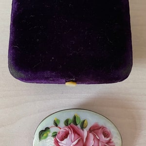 May include: A silver oval brooch with a white enamel background and hand-painted pink roses with green leaves.