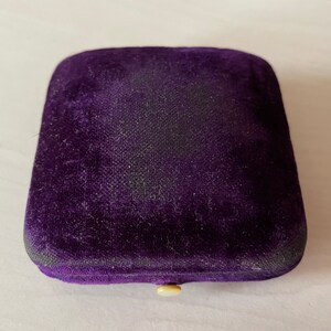 May include: A purple velvet jewellery box with a white button closure.