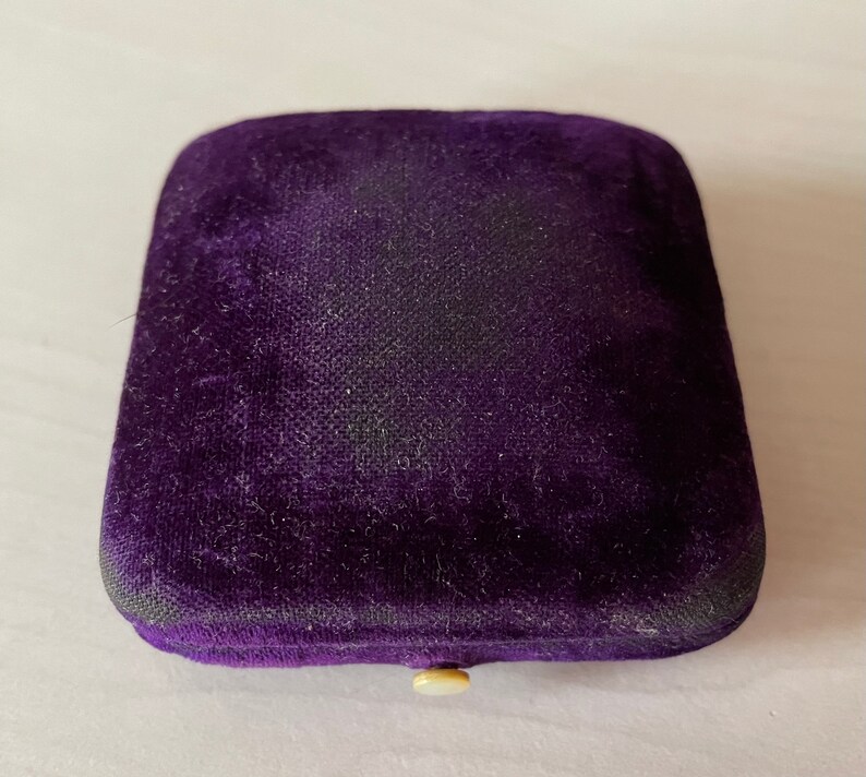 May include: A purple velvet jewellery box with a white button closure.