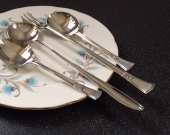 May include: Three silver spoons with ornate handles on a white plate with a floral design. The spoons are arranged in a row, with the largest spoon at the bottom and the smallest spoon at the top.