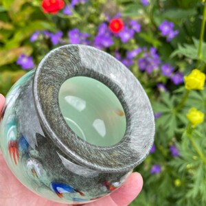 K&ouml;nnte beinhalten: Eine kleine, runde Glassch&uuml;ssel mit einem gr&uuml;n-wei&szlig;en Wirbelmuster. Die Sch&uuml;ssel hat einen dunkelgrauen Rand und ein hellgr&uuml;nes Inneres.