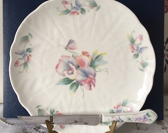 May include: A white ceramic serving platter with a floral design featuring pink, blue, and green sweet pea flowers. The platter comes with a matching knife with a silver blade and a white handle with a floral design.
