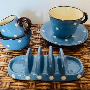 May include: A blue and white polka dot tea set with a teapot, creamer, sugar bowl, and a toast rack. The set is made of ceramic and has a rustic, vintage look.