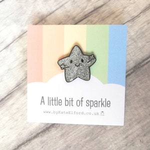 May include: A sparkly silver star-shaped brooch with a smiling face and outstretched arms, presented on a card with a rainbow gradient. The card reads "A little bit of sparkle" and a website address.