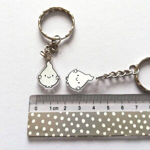 Two silver keychains with clear acrylic charms shaped like flames with black outlines and smiling faces. The charms are approximately 2.5 cm in size. The keychains are on a white surface with a ruler for scale.
