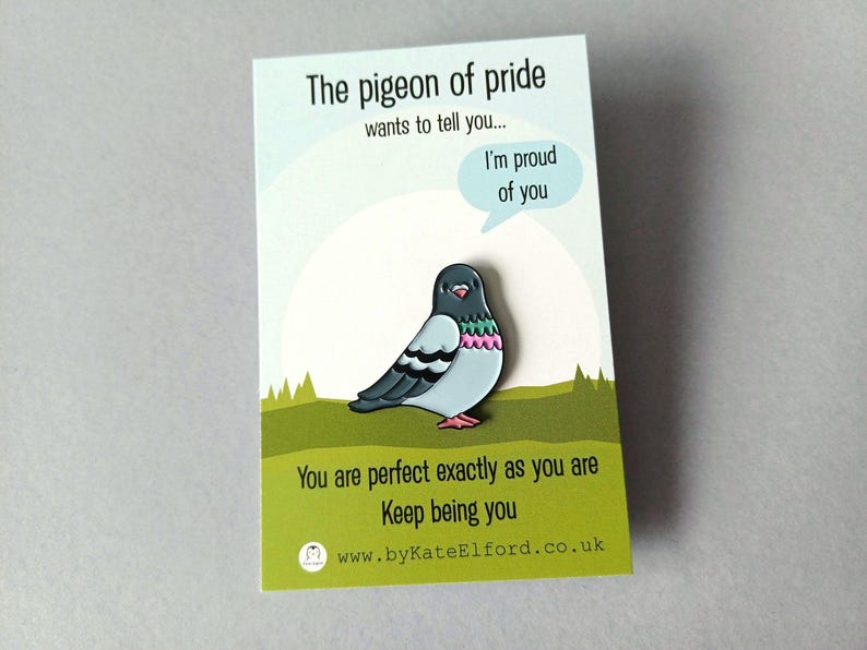 A pin badge of a cartoon pigeon with a speech bubble saying "I'm proud of you." The badge is on a card with the text "The pigeon of pride wants to tell you..." and "You are perfect exactly as you are. Keep being you."