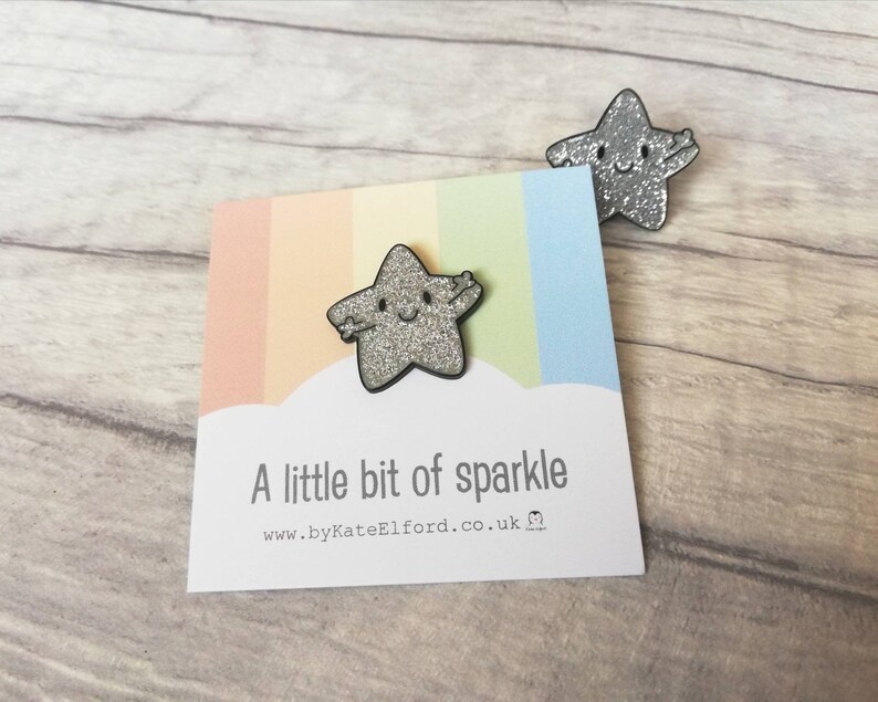 May include: Two silver glitter star-shaped pins with smiling faces. One pin is attached to a card with a rainbow background and the text "A little bit of sparkle". The website address www.byKateElford.co.uk is also visible.