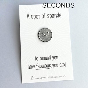 May include: A white card with black text that reads "SECONDS", "A spot of sparkle", "to remind you", "how fabulous you are!" and "www.byKateElford.co.uk". A silver glitter pin with a smiley face is attached to the card.