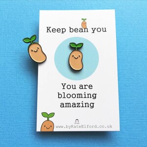 May include: A white card with the text "Keep bean you" and "You are blooming amazing" with a small bean sprout illustration. The card is on a blue background with two bean sprout pins.