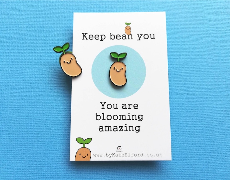 May include: A white card with the text "Keep bean you" and "You are blooming amazing" with a small bean sprout illustration. The card is on a blue background with two bean sprout pins.