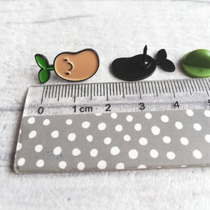 May include: Three enamel pins: a green sprout growing from a brown potato, a black whale, and a green button.