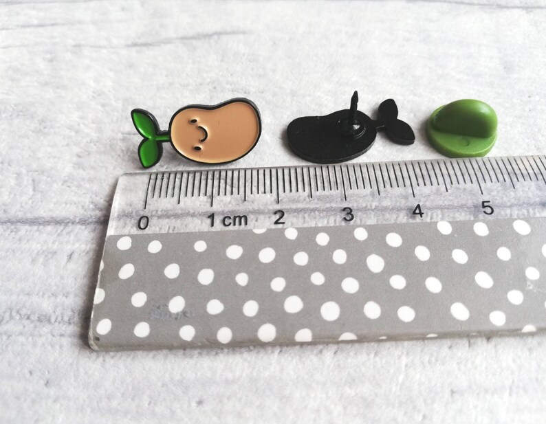 May include: Three enamel pins: a green sprout growing from a brown potato, a black whale, and a green button.