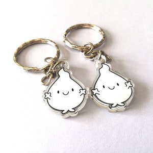 Two silver keyrings with clear acrylic charms shaped like flames with smiling faces. The flames have small arms and legs.
