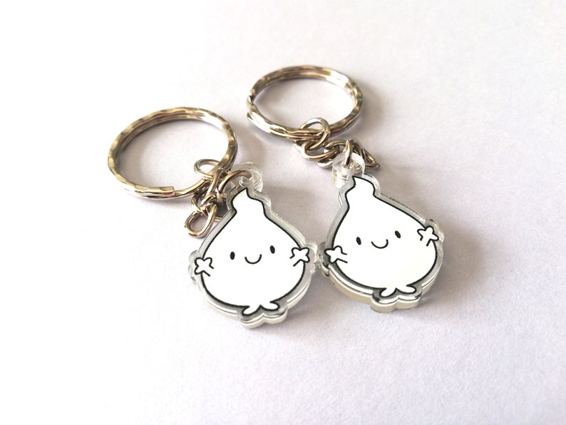 Two silver keyrings with clear acrylic charms shaped like flames with smiling faces. The flames have small arms and legs.