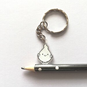 A white flame keyring with a smiling face and a silver key ring. The keyring is hanging from a pencil with black and white polka dots.