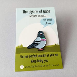 A colourful pigeon enamel pin on a backing card. The card reads "The pigeon of pride wants to tell you... I'm proud of you." and "You are perfect exactly as you are. Keep being you." The pin is a cute, positive design.