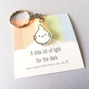 A silver keyring with a small, white flame charm. The charm has a happy face. The keyring comes with a card that reads "A little bit of light for the dark".