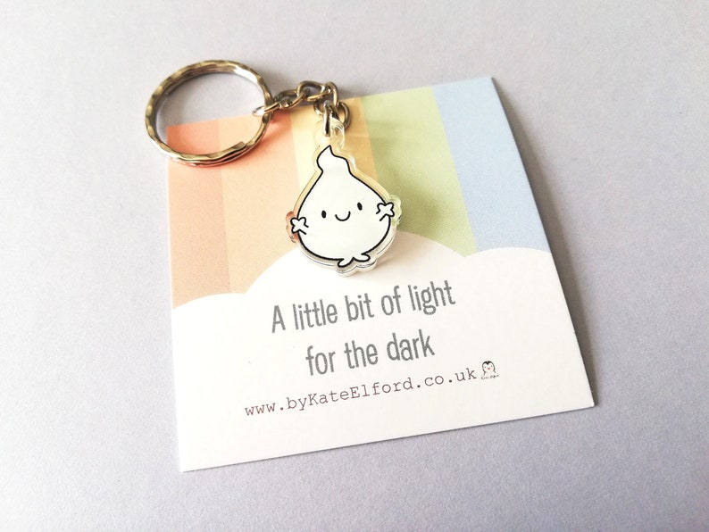 A silver keyring with a small, white flame charm. The charm has a happy face. The keyring comes with a card that reads "A little bit of light for the dark".