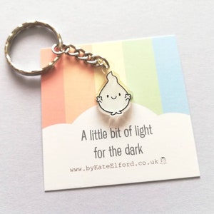 A silver keychain with a small white ghost charm that says "A little bit of light for the dark".