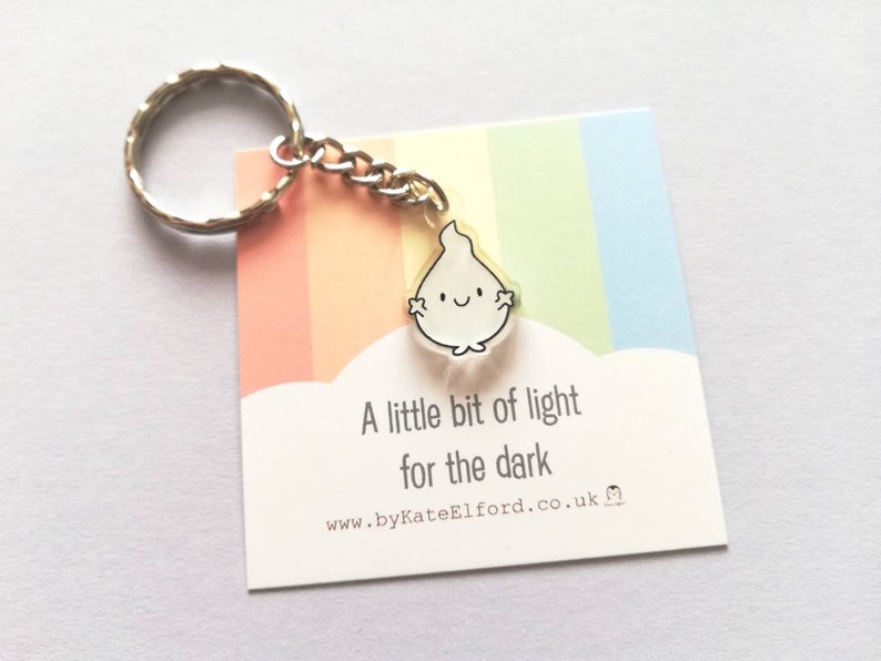 A silver keychain with a small white ghost charm that says "A little bit of light for the dark".