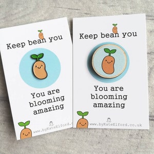 May include: Two white cards with blue accents and a cartoon bean sprout illustration. The text on the cards reads "Keep bean you. You are blooming amazing." and includes the website address "www.byKateElford.co.uk".