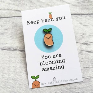 May include: A white card with the text "Keep bean you, you are blooming amazing" and a cartoon bean sprout with a smiling face. The card also includes the website address "www.byKateElford.co.uk".