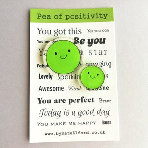 Puede incluir: Una tarjeta con el texto "Pea of positivity" y otras afirmaciones positivas. Dos amuletos verdes en forma de guisante con caras sonrientes est&aacute;n en la tarjeta. El sitio web www.byKateElford.co.uk est&aacute; en la parte inferior.