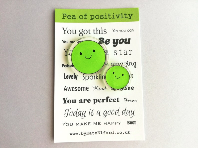 Puede incluir: Una tarjeta con el texto "Pea of positivity" y otras afirmaciones positivas. Dos amuletos verdes en forma de guisante con caras sonrientes est&aacute;n en la tarjeta. El sitio web www.byKateElford.co.uk est&aacute; en la parte inferior.