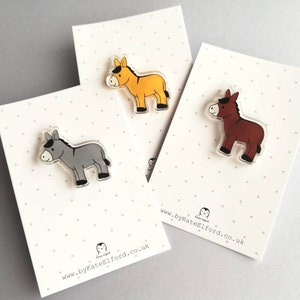 May include: Three donkey pins, one gray, one yellow, and one brown. Each pin is on a white card with black polka dots and the text "www.byKateElford.co.uk".