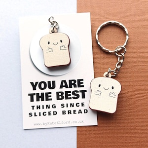 May include: A wooden bread slice keyring with a smiling face and arms. The keyring is attached to a silver ring. The card behind the keyring reads "YOU ARE THE BEST THING SINCE SLICED BREAD".