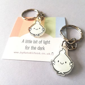 Two silver keyrings with a clear, white flame charm. The flame has a smiling face and small arms. The charms are attached to silver key rings. The keyrings are displayed on a card with the text "A little bit of light for the dark".
