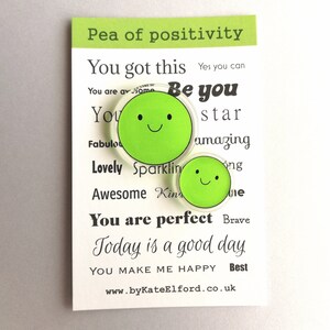 Puede incluir: Dos imanes verdes con forma de guisante y caras sonrientes se muestran en una tarjeta blanca. La tarjeta tiene el texto "Pea of positivity" y frases motivadoras como "You got this" y "Today is a good day."