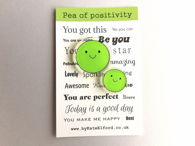 Puede incluir: Dos imanes verdes con forma de guisante y caras sonrientes se muestran en una tarjeta blanca. La tarjeta tiene el texto "Pea of positivity" y frases motivadoras como "You got this" y "Today is a good day."