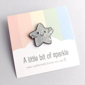 A silver glitter star pin, with a happy face and arms held out for a hug. The backing card has a rainbow background with the wording a little bit of sparkle