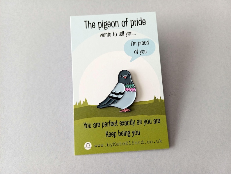A colourful pigeon pin on a card. The card reads "The pigeon of pride wants to tell you... I'm proud of you." and "You are perfect exactly as you are." The pin is a cartoon design with a speech bubble.