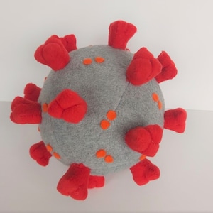 May include: A gray plush toy shaped like a coronavirus with red spikes and orange dots.