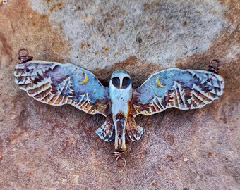 May include: A handcrafted owl pendant with outstretched wings, featuring a detailed design of a night sky with crescent moons and trees. The owl is painted in shades of blue, brown, and white, with copper wire accents for hanging. A unique piece of jewellery.