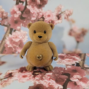 Pode incluir: Um urso de peluche marrom com uma barriga de botão em pé em um fundo floral rosa e branco.