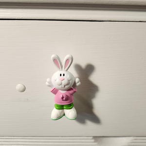 May include: White bunny rabbit drawer pull with pink shirt and green pants.