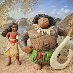 May include: A brown and tan plastic action figure of Maui from the film Moana, holding a large white hook. He is wearing a green grass skirt and a necklace of white teeth. A brown and tan plastic action figure of Moana is standing next to him. She is wearing a brown and tan dress and a blue necklace.