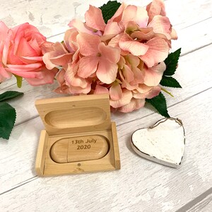 May include: A wooden box with a hinged lid, containing a small wooden USB drive engraved with the date "13th July 2020". The box is open and the USB drive is visible. A white heart-shaped ornament is in the background.