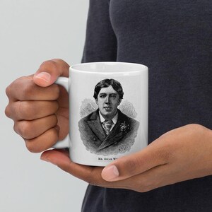 Pu&ograve; includere: Una tazza in ceramica bianca con un'immagine in bianco e nero di Oscar Wilde. L'immagine mostra Wilde in abito e cravatta con un fiore all'occhiello. Il testo "MR. OSCAR WILDE" &egrave; stampato sotto l'immagine.